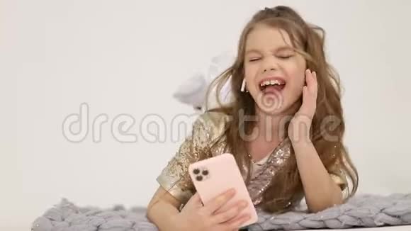 小女孩在智能手机上听音乐女孩在家里的床上唱歌视频的预览图