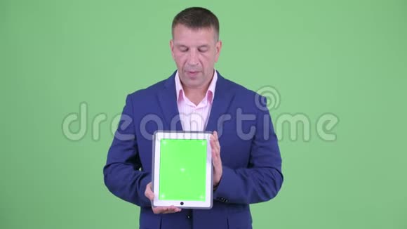 成熟有男子气概的商人在展示数码平板电脑的同时还会说话视频的预览图