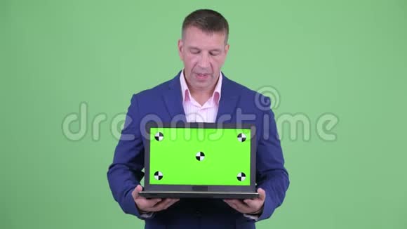 成熟有男子气概的商人在展示笔记本电脑的同时还会说话视频的预览图