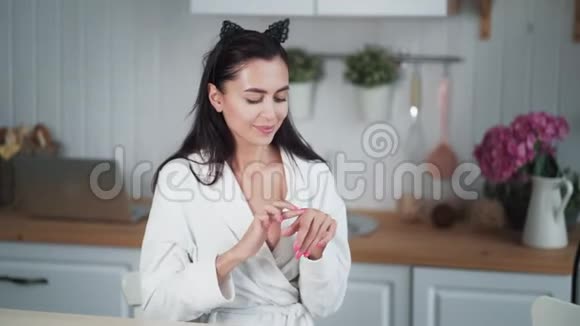 穿浴袍的女人的肖像在她的脸上涂上奶油做面部按摩视频的预览图