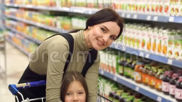 妈妈和女儿在超市玩得开心女孩坐在购物车里视频的预览图