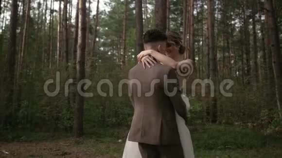 当新婚夫妇在树林里旋转时动作缓慢美丽的森林里美丽的年轻婚礼夫妇拥抱亲吻视频的预览图