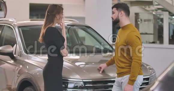 年轻的高加索夫妇站在汽车经销商和选择新的汽车成功的男人和女人买车视频的预览图