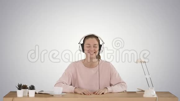 漂亮的女士穿着粉红色套头衫听着耳机里的音乐微笑着在渐变背景下拍摄视频的预览图