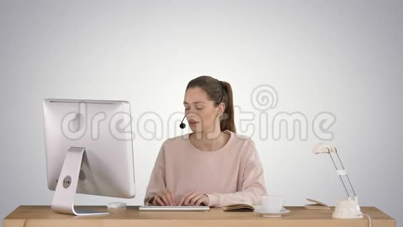 漂亮的年轻休闲女士戴着耳机在渐变背景下在电脑上工作视频的预览图