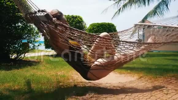 一位身穿泳装的年轻美女躺在吊床上围着热带植物享受假期视频的预览图