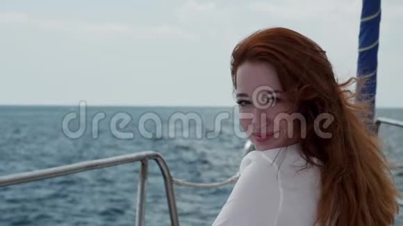 一个红头发的女孩坐在一艘游艇的船头上它在海上航行微笑着看着你视频的预览图