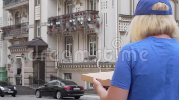 一位送货员拿着披萨盒在街上四处张望的后景镜头视频的预览图