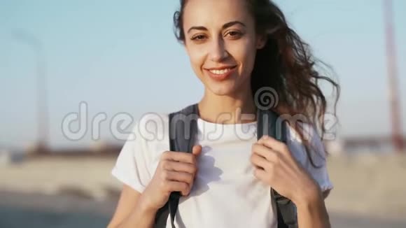 幸福微笑的年轻美女穿着白色t恤站在蓝天背景上的桥上手伸直视频的预览图