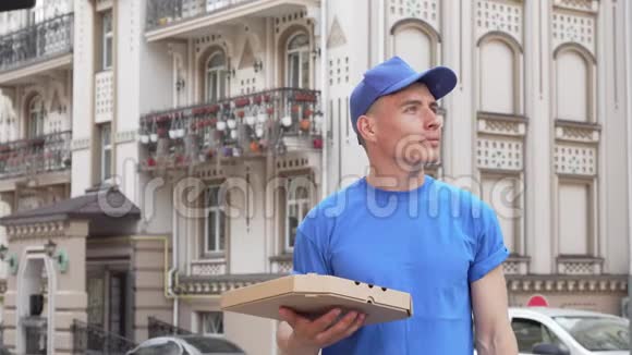 快乐的披萨快递员在城市街上环顾四周后微笑着对着相机视频的预览图