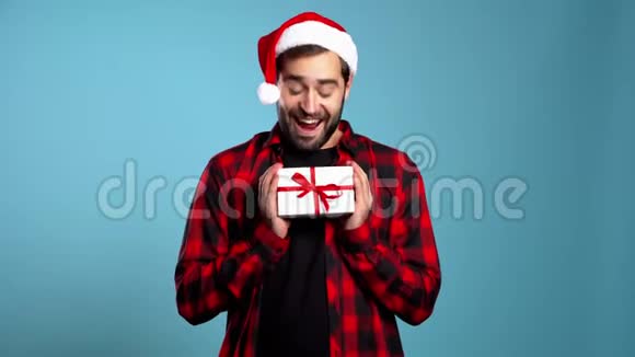 年轻的帅哥微笑着拿着礼品盒在蓝色的工作室背景上视频的预览图