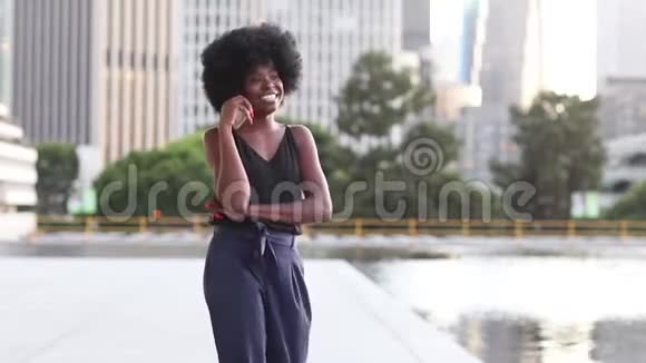 年轻的非洲妇女在喷泉边与城市背景的摩天大楼通话视频的预览图