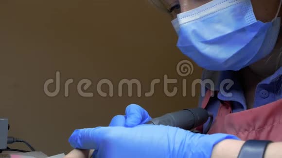 在一家美容店为一位女士做五金指甲的美甲师的面部特写医生从指甲中去除角质层慢慢视频的预览图