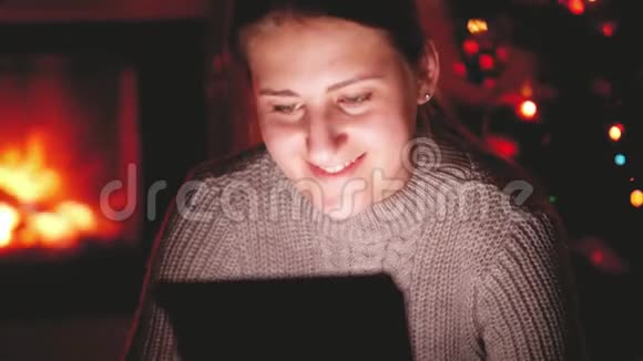 带着微笑的年轻女子在客厅里的平板电脑上观看视频在燃烧的壁炉里视频的预览图