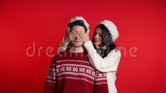 女人闭上心爱的男朋友的眼睛然后给他惊喜戴着圣诞帽的夫妇视频的预览图