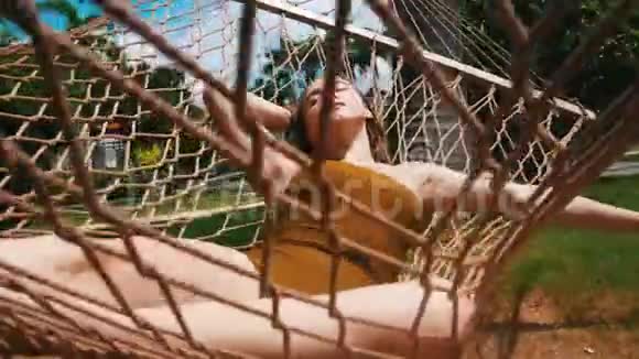 一个年轻漂亮的女人躺在吊床上闭着眼睛看着热带植物休息一下视频的预览图