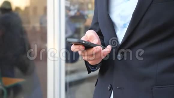 成功的商人穿着西装站在城市街道和浏览智能手机自信的人打字或使用视频的预览图
