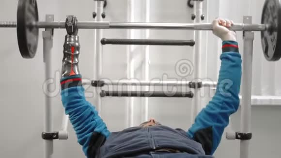 没有手的运动员在躺下时举起杠铃用一个专业的运动手假体托住杆视频的预览图