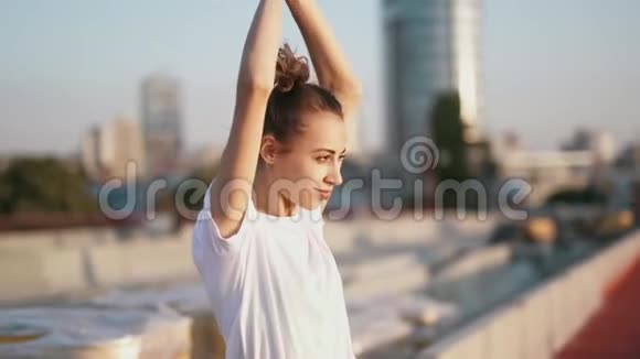 一位身穿白色t恤笑容满面的年轻漂亮女子举手站在城市背景的桥上视频的预览图