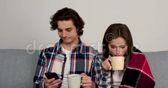 一对幸福的夫妇坐在沙发上喝茶用智能手机视频的预览图