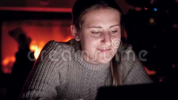 4K年轻女子的肖像穿着毛衣晚上使用数码平板电脑客厅里有燃烧的火焰视频的预览图