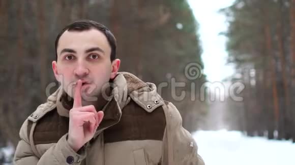 穿夹克的年轻人的肖像正在做沉默的手势人站在冬林中视频的预览图