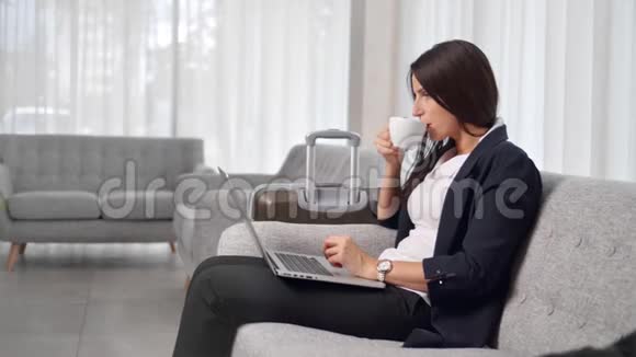 自信的女商人在商务旅行中喝咖啡或茶使用笔记本电脑工作视频的预览图