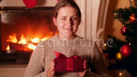 圣诞前夜一位微笑的年轻女子坐在客厅里并在镜头中展示圣诞老人的礼物视频的预览图