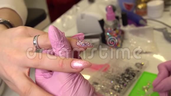 用美甲师把莱茵石贴在画好的指甲化妆品和指甲上的宏景镜头接近指甲视频的预览图