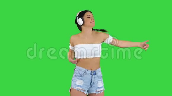 高加索女模特戴着耳机跳跃在绿色屏幕上表达快乐的情绪Chroma键视频的预览图