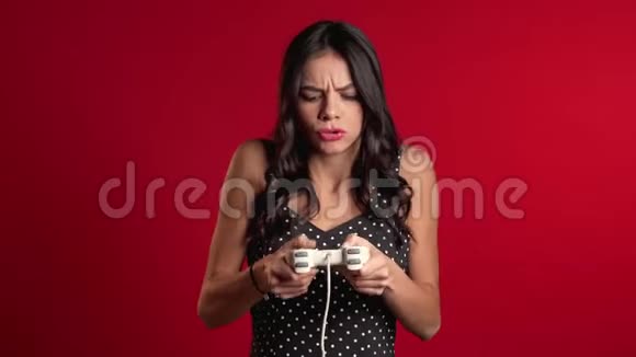 漂亮的拉丁女孩在TV上玩电子游戏红色工作室墙上有操纵杆利用现代技术视频的预览图