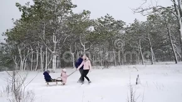 幸福的家庭在下雪的冬天滑雪女儿帮助父亲和母亲在下雪时和儿子拉雪橇男孩视频的预览图