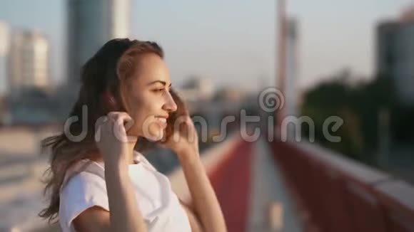 幸福微笑的年轻美女穿着白色t恤站在蓝天背景上的桥上手伸直视频的预览图