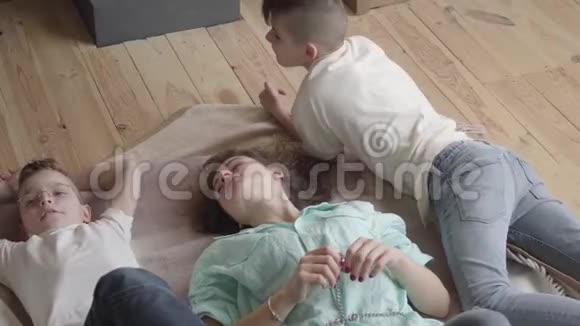 年轻的母亲和她的十几岁的儿子躺在地板上孩子们的房间里交谈分享与孩子们交流一个男孩视频的预览图