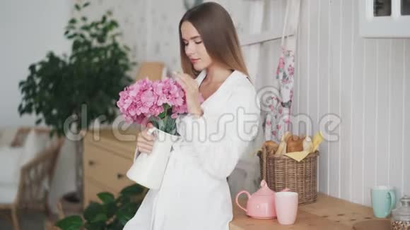快乐的年轻女子穿着白色浴袍捧着一束鲜花嗅着它微笑着视频的预览图