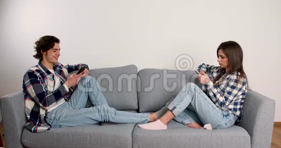 一对牛仔裤使用智能手机坐在客厅沙发上微笑视频的预览图