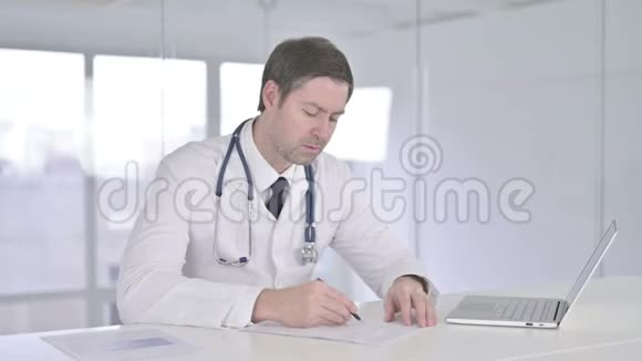 严重中年医生在办公室做文书工作视频的预览图