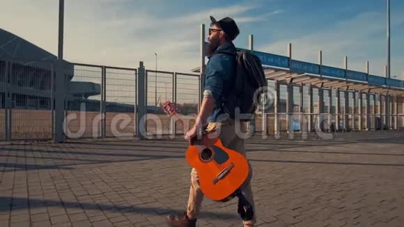 一个阳光明媚的日子里带着吉他在公园里散步的哈普斯特胡子男音乐家双眼黝黑温暖视频的预览图