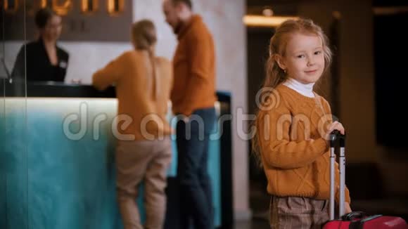 一家人在豪华酒店登记一个小女孩拿着手提箱站在那里等她的父母视频的预览图