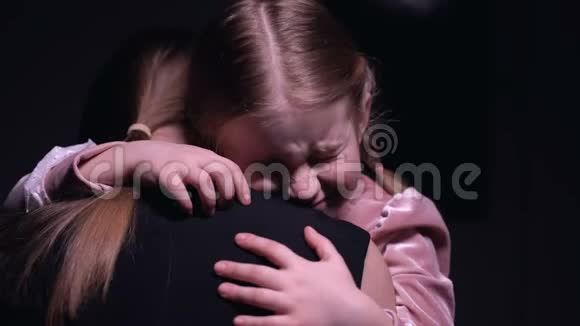 害怕的女孩拥抱母亲在黑色背景下惊恐地哭泣视频的预览图