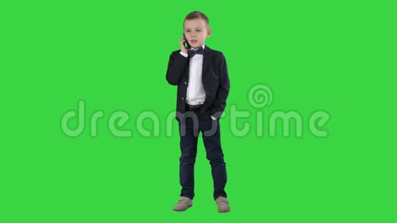可爱的小男孩在他的智能手机上说话站在一个黑暗的西装绿色屏幕Chroma键视频的预览图