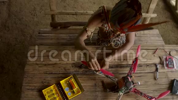 一个年轻的土著人正在他的乡村小屋里建造一架无人机视频的预览图