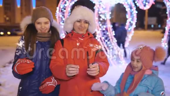在圣诞前夜母亲带着两个女儿在市中心的一个有趣的夜晚手里拿着闪闪发光的东西视频的预览图