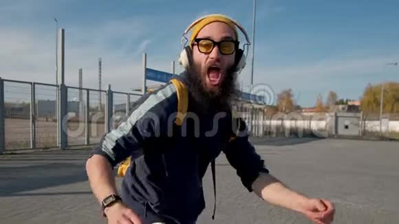 一个穿着黄色衣服戴耳机欣赏音乐的时髦留胡子男人的肖像蓝蓝的天空背景视频的预览图