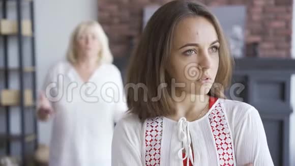 前景中年轻女子的肖像她的母亲在背景中进行情感上的手势年轻女子在争吵视频的预览图