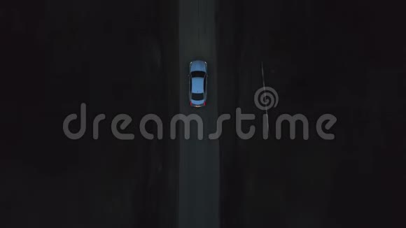 高空俯瞰银色高级轿车凯迪拉克CT在黑暗的乡村道路上行驶在夏季森林中的夜晚视频的预览图