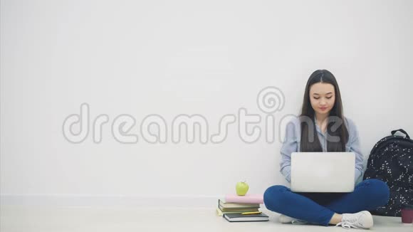 可爱的年轻亚洲女士坐在地板上以洛托斯的姿势在互联网上搜索挥手问好学校用品视频的预览图