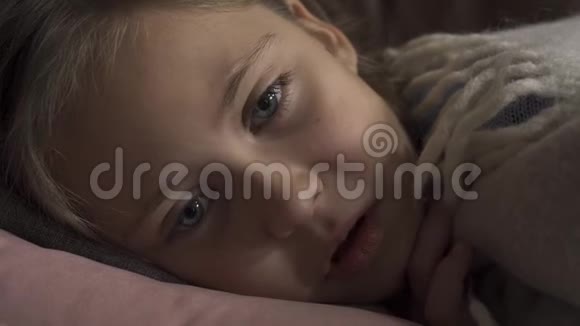 一个生病的白种人女孩躺在家里的毯子下咳嗽的特写脸这个悲伤的孩子发烧了概念视频的预览图