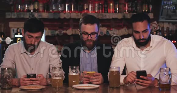 三个老朋友坐在啤酒酒吧里用智能手机传播网络成瘾的概念视频的预览图