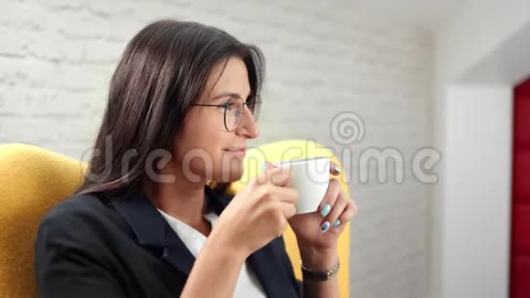 微笑着美丽的非正式商务女性在白色房间背景下放松地喝咖啡视频的预览图